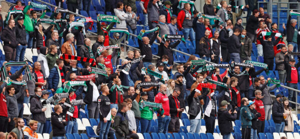 Fans auf den Tribünen des Stadions halten bunte Schals hoch und feuern ihre Mannschaft Hannover 96 an.