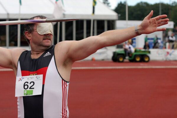 Ein sehbehinderter Athlet mit einer Augenbinde wirft bei einem Leichtathletikwettkampf einen Speer.